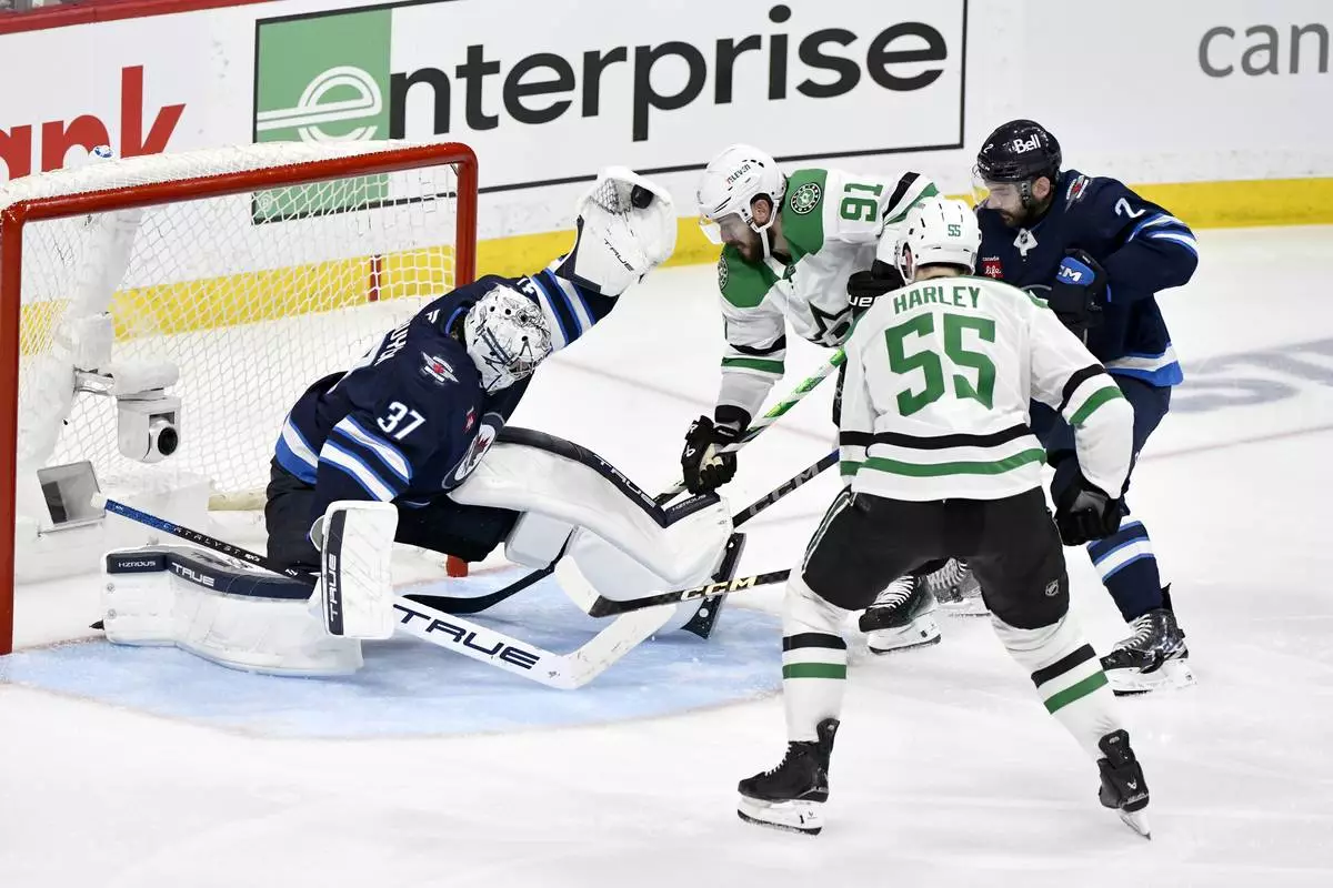 Winnipeg Jets goaltender Connor Hellebuyck (37) makes a save on a Dallas Stars shot as Tyler Seguin (91) and Thomas Harley (55) look for the rebound during second period NHL playoff hockey action in Winnipeg, Thursday, May 15, 2025. (Fred Greenslade/The Canadian Press via AP)