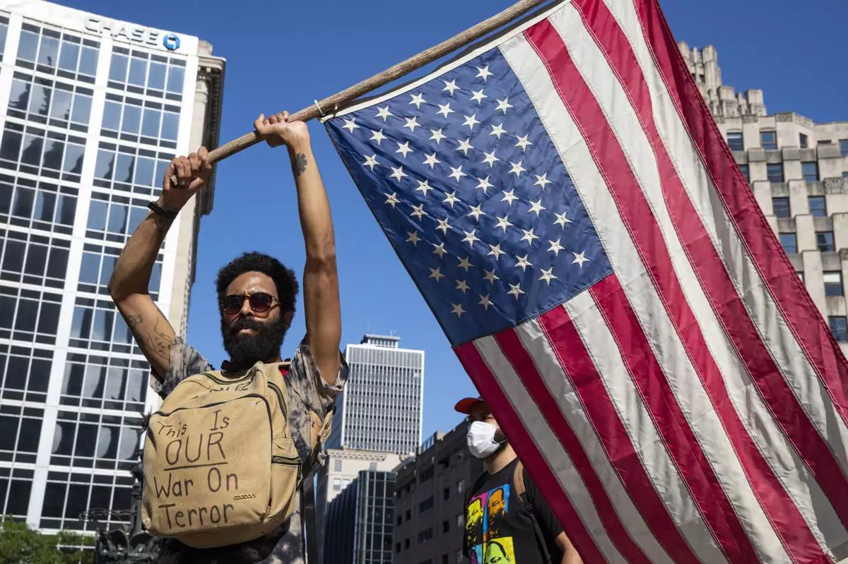 A protester holds a U.S. flag at Monument Circle following a non-violent sit-in at the Statehouse in Indianapolis, Saturday, June 6, 2020, against police brutality sparked by the death of George Floyd. (AP Photo/Michael Conroy, File)