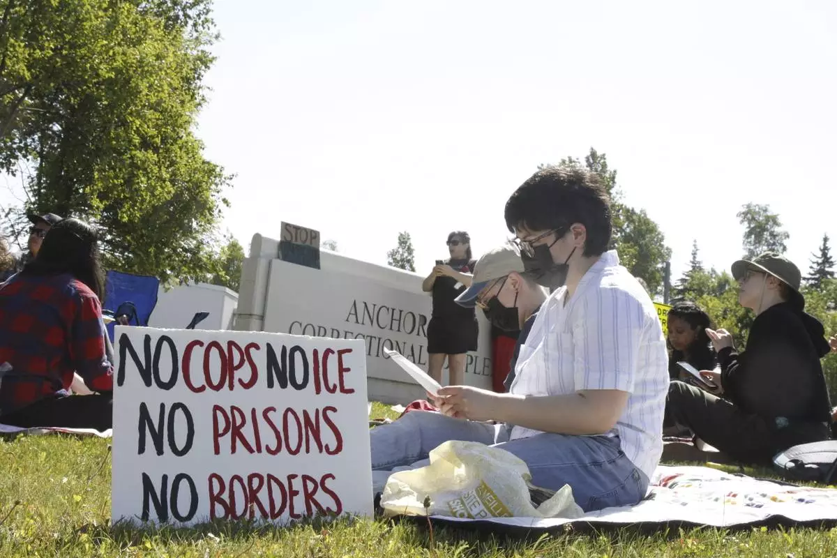 Demonstrators sit on the lawn of the Anchorage Correctional Complex Thursday, June 12, 2025, in Anchorage, Alaska, to protest the detainment of about 40 people being held there under the custody of the Immigration and Customs Enforcement federal agency. (AP Photo/Mark Thiessen)