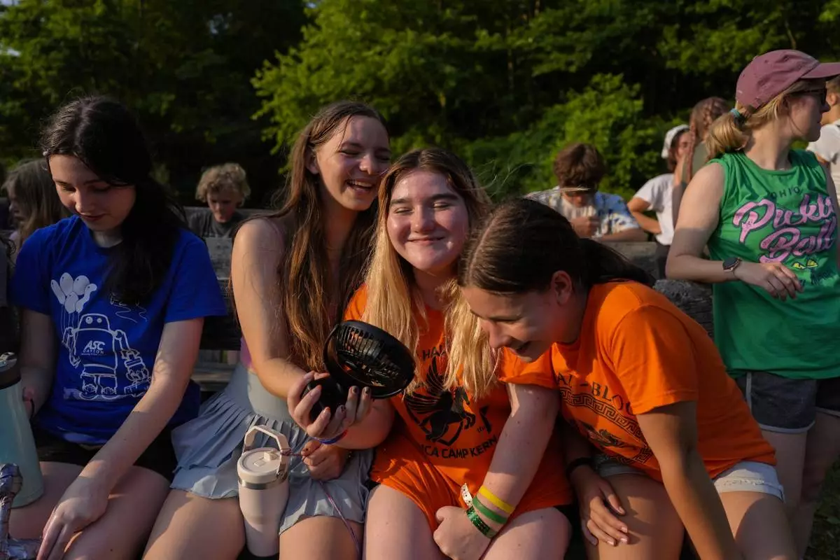 FILE - Mirabelle Demske, second from left, uses a portable electric fan to cool off her friends Faith Hamzy, center, and Annie Sayre, second from right, June 20, 2024, at YMCA Camp Kern in Oregonia, Ohio. (AP Photo/Joshua A. Bickel, File)