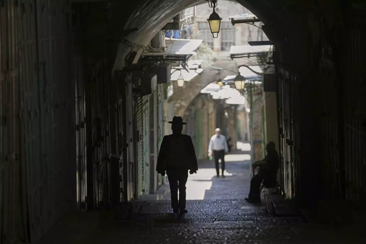 People walk in an nearly empty alley in Jerusalem's Old City as Israel's Home Front Command banned public gatherings following an Israeli military strike on Iran, in Jerusalem's Old City, Friday, June 13, 2025. (AP Photo/Mahmoud Illean)
