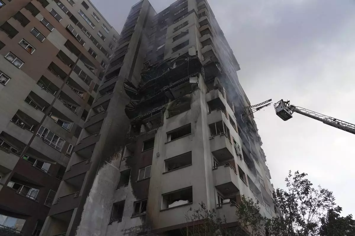 A firefighter stands on a crane at the scene of an explosion at a residence compound after Israeli attacks in Tehran, Friday, June 13, 2025. (AP Photo/Vahid Salemi)