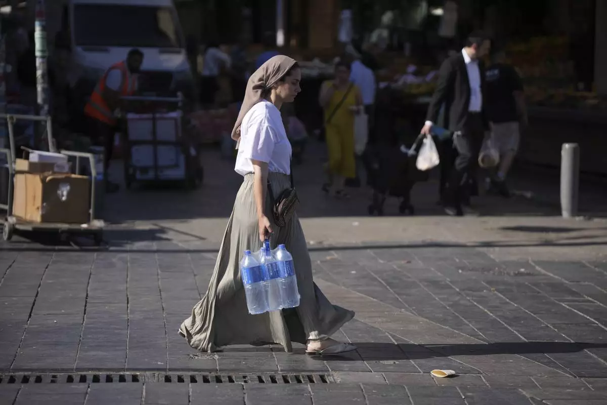A woman carries water at the Mahane Yehuda market in Jerusalem ahead of Shabbat, Friday, June 13, 2025. (AP Photo/Ohad Zwigenberg)