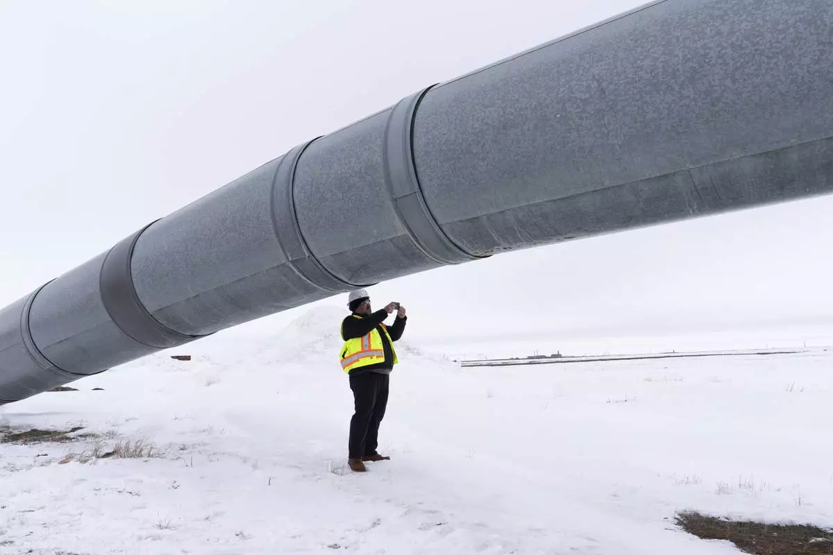 A worker takes a photo under the start of the Trans-Alaska Pipeline after a news conference at the Pump Station 1 on Monday, June 2, 2025, located near Deadhorse, Alaska, on the state's prodigious North Slope. (AP Photo/Jenny Kane)