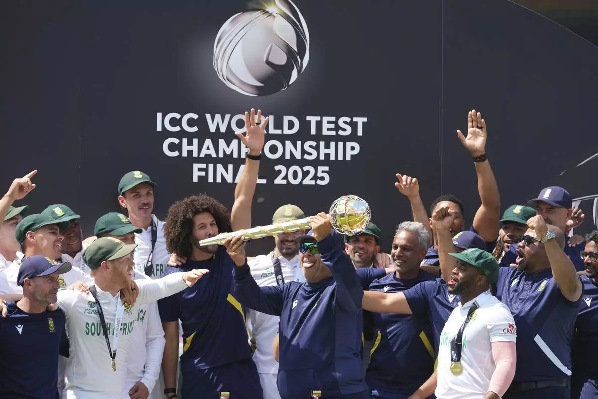South Africa's head coach Shukri Conrad holds the winner's trophy and celebrates with players on the podium after their win in the World Test Championship final against Australia at Lord's cricket ground in London, Saturday, June 14, 2025. (AP Photo/Kirsty Wigglesworth)