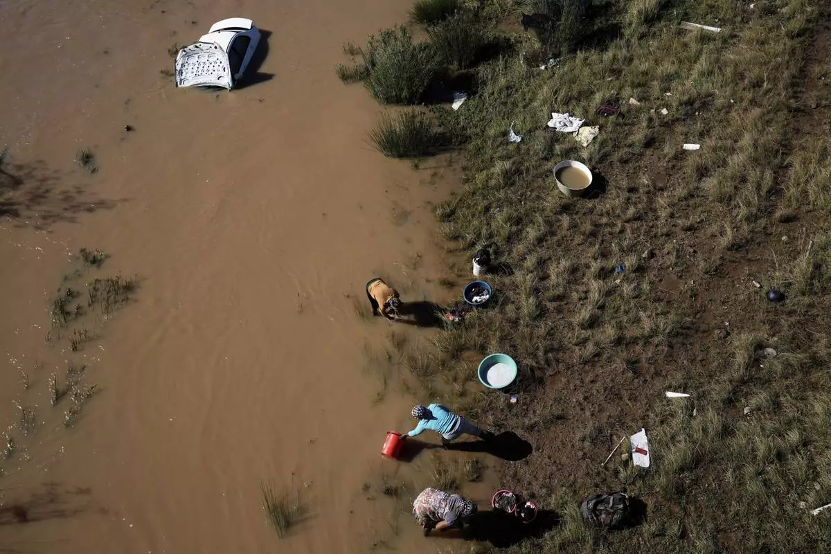 Women wash their clothes along the river next a car that was swept through by floods in Mthatha, South Africa, Thursday, June 12, 2025. (AP Photo/Themba Hadebe)