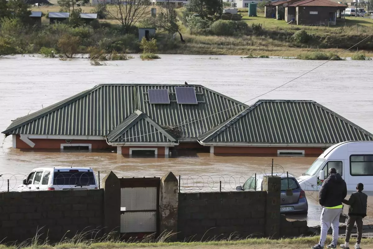 A man with a child look at a home submerged in floodwater, in Mthatha, South Africa, Tuesday, June 10, 2025. (AP Photo/Hoseya Jubase)