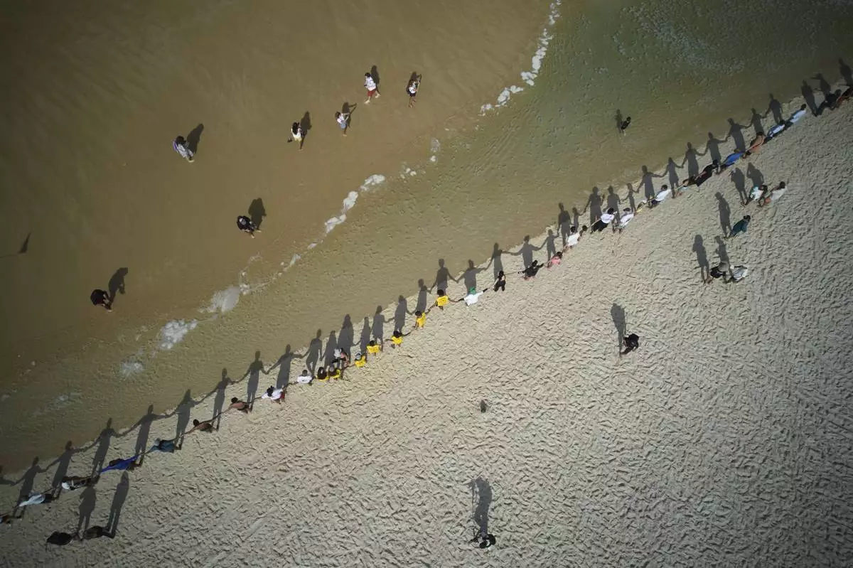 People hold hands along Sao Conrado beach for a symbolic group hug with the sea on World Oceans Day, in Rio de Janeiro, June 8, 2025. (AP Photo/Silvia Izquierdo)
