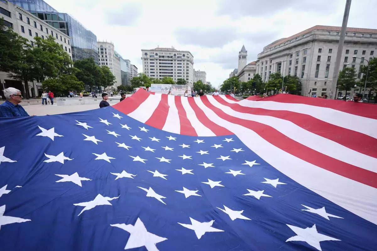 People hold a large American flag at Freedom Plaza before a parade commemorating the Army's 250th anniversary, coinciding with President Donald Trump's 79th birthday, Saturday, June 14, 2025, in Washington. (AP Photo/Manuel Balce Ceneta)