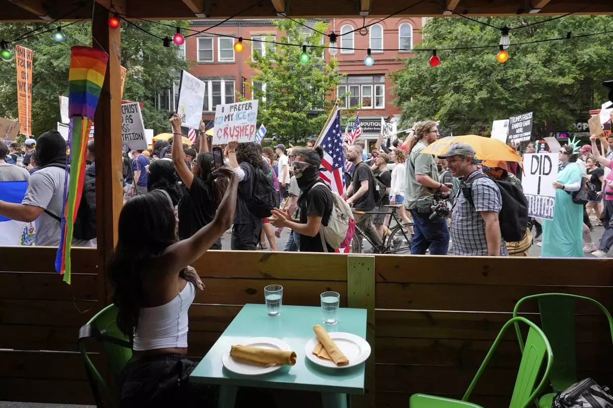 A person sitting in a restaurant records demonstrators as they march during a protest taking place on the day of a military parade commemorating the Army's 250th anniversary, coinciding with President Donald Trump's 79th birthday, Saturday, June 14, 2025, in Washington. (AP Photo/Alex Brandon)