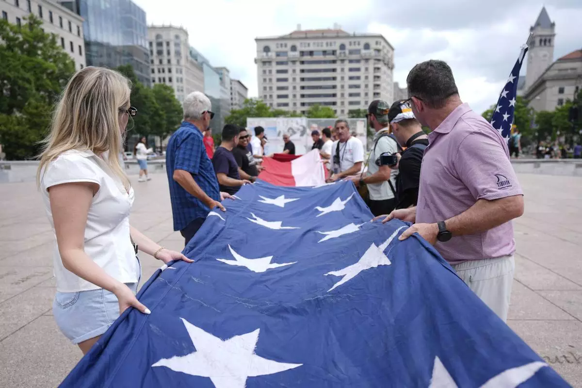 People fold a large American flag at Freedom Plaza before a parade commemorating the Army's 250th anniversary, coinciding with President Donald Trump's 79th birthday, Saturday, June 14, 2025, in Washington. (AP Photo/Manuel Balce Ceneta)
