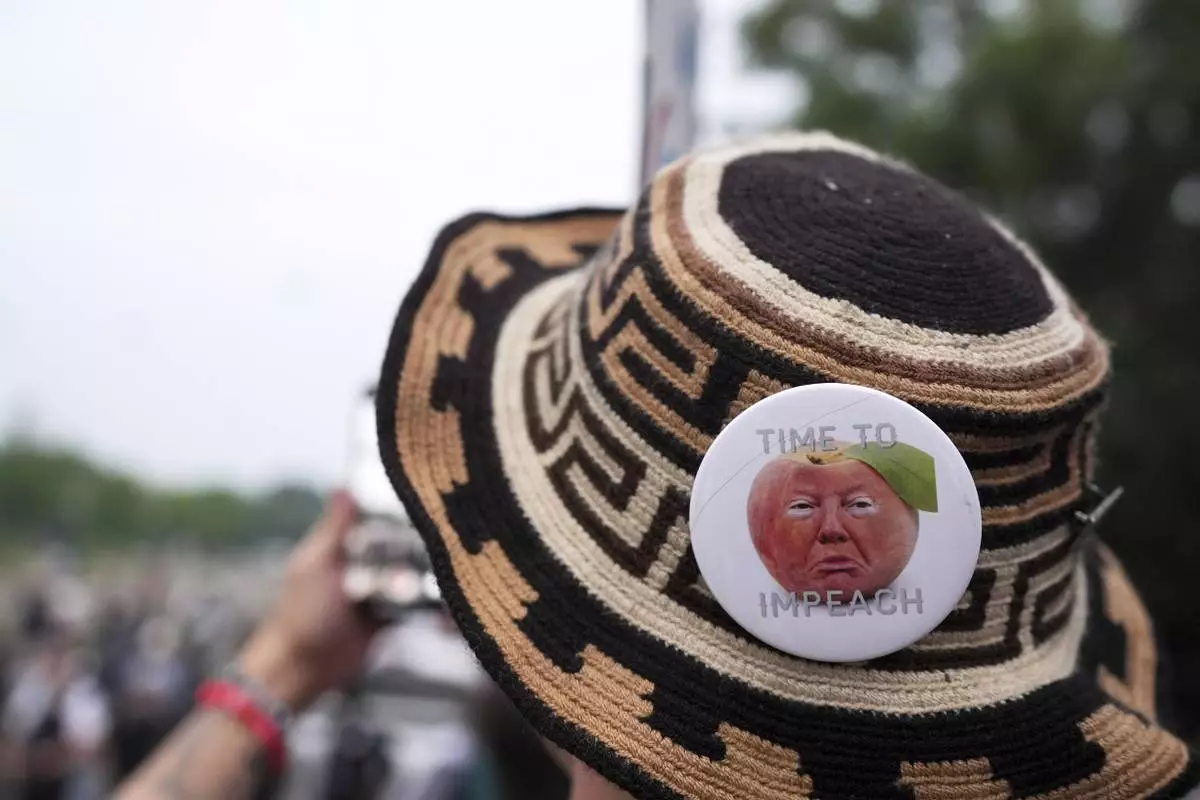 A demonstrator wears a pin stating "time to impeach" during a protest taking place on the day of a military parade commemorating the Army's 250th anniversary, coinciding with President Donald Trump's 79th birthday, Saturday, June 14, 2025, in Washington. (AP Photo/Evan Vucci)