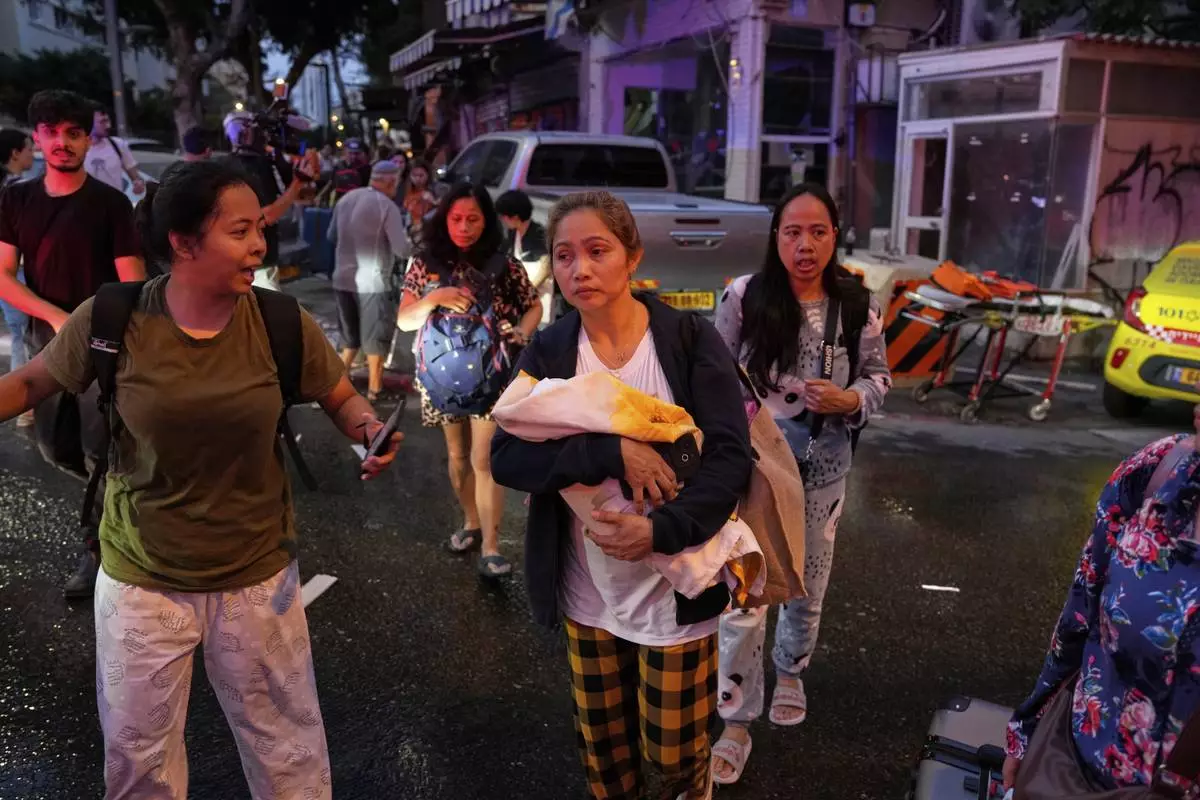 A woman holds her baby as residents evacuate the area after a missile launched from Iran struck in downtown Tel Aviv, Israel, Monday June 16, 2025. (AP Photo/Baz Ratner)