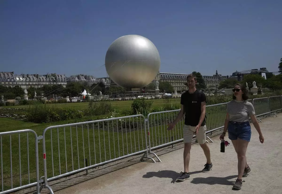 People walk past the Olympic cauldron at the Tuileries Gardens, ahead of its nightly summer relaunch starting June 21, in Paris, Thursday, June 12, 2025. (AP Photo/Michel Euler)