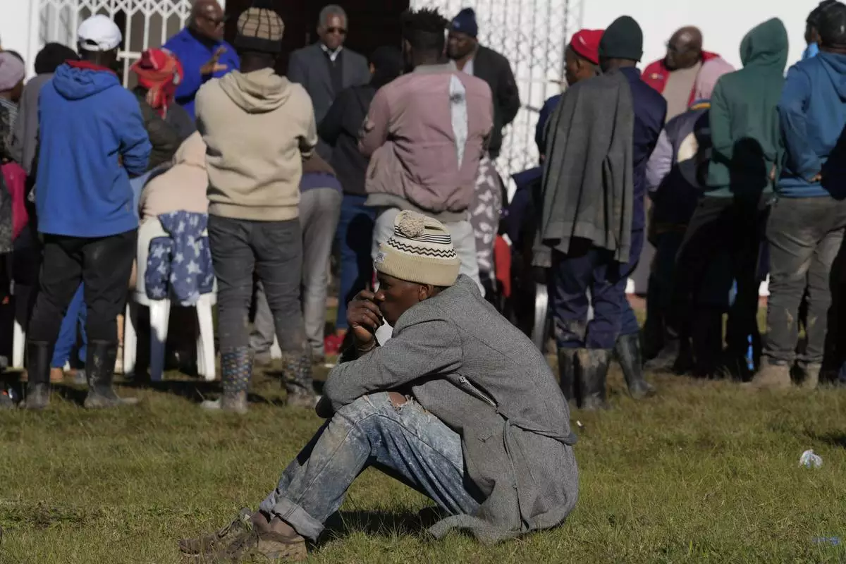 A man sits on the ground as a minister addresses flood victims outside a temporary shelter at a church following floodsin Mthatha, South Africa, Thursday, June 12, 2025. (AP Photo/Themba Hadebe)