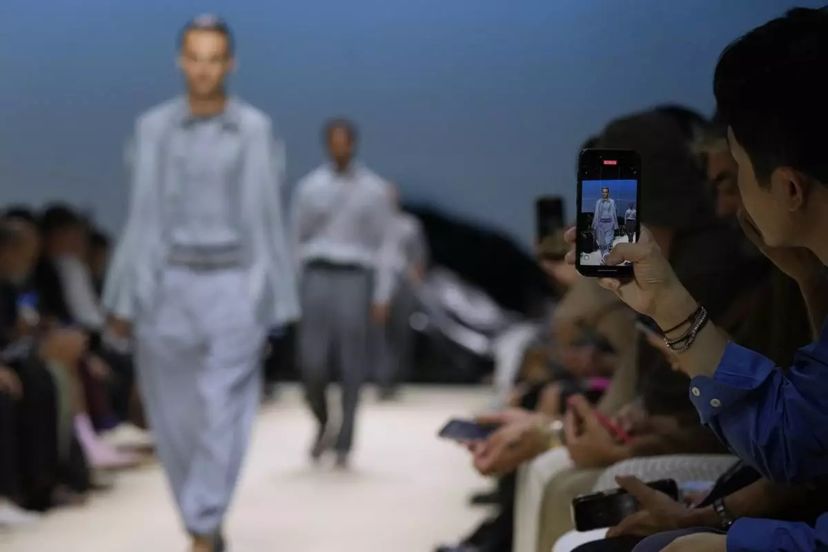 A guest takes a photograph during the men's Giorgio Armani Spring-Summer 2026 collection, that was presented in Milan, Italy, Monday, June 23, 2025. (AP Photo/Luca Bruno)