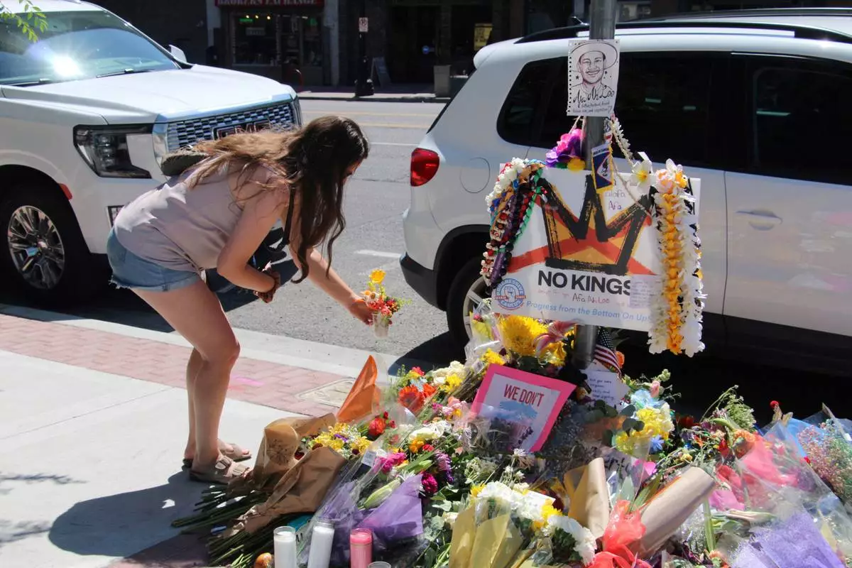 A woman lays flowers Tuesday, June 17, 2025, at a makeshift memorial for Arthur Folasa Ah Loo, known to friends and family as Afa, on the city block in Salt Lake City, where Ah Loo was fatally shot during a "No Kings" protest on Saturday, June 14. (AP Photo/Hannah Schoenbaum)