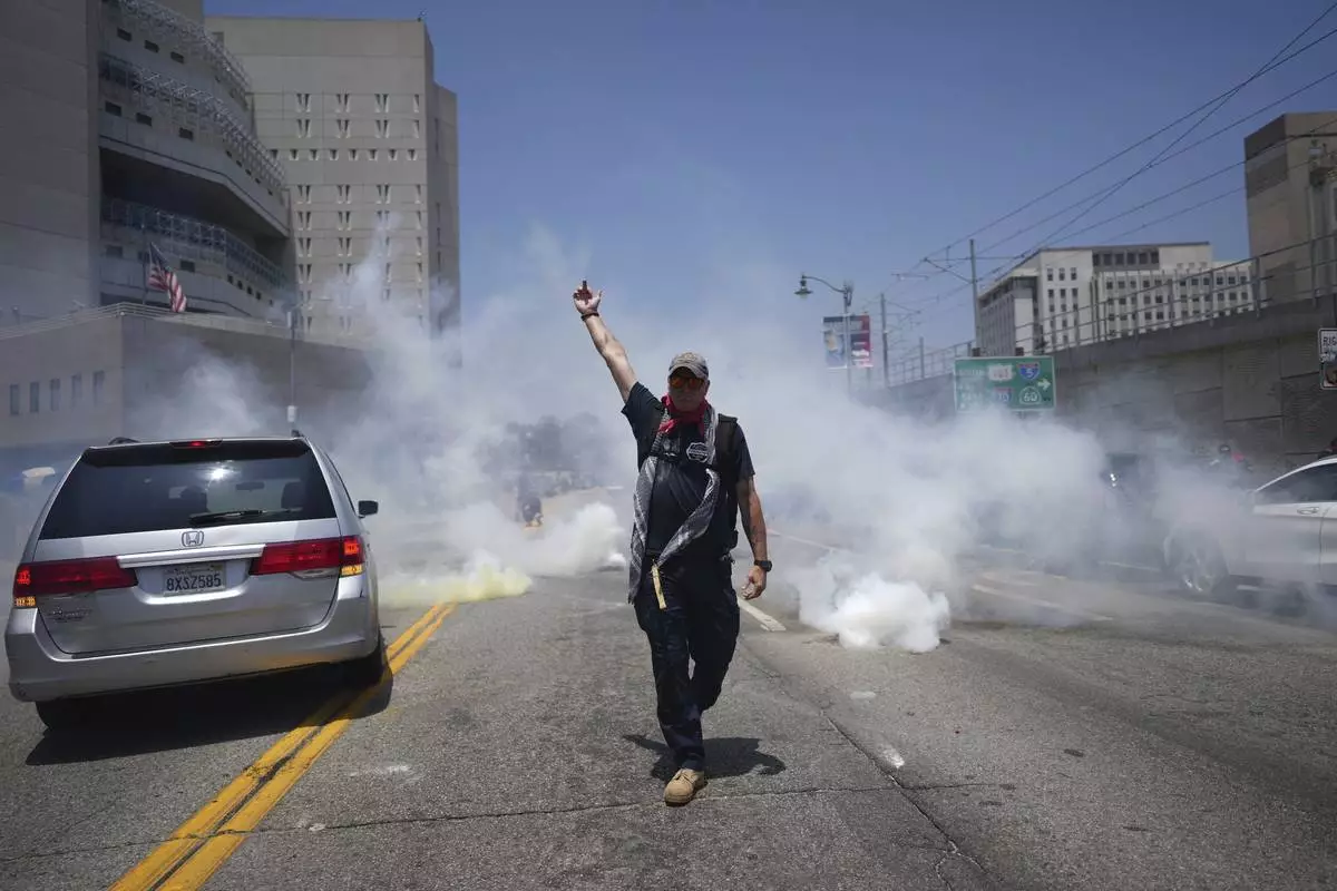 EDS NOTE: OBSCENITY - A protester gestures as tear gas is used near the Metropolitan Detention Center in downtown Los Angeles, Sunday, June 8, 2025, following last night's immigration raid protest. (AP Photo/Eric Thayer)