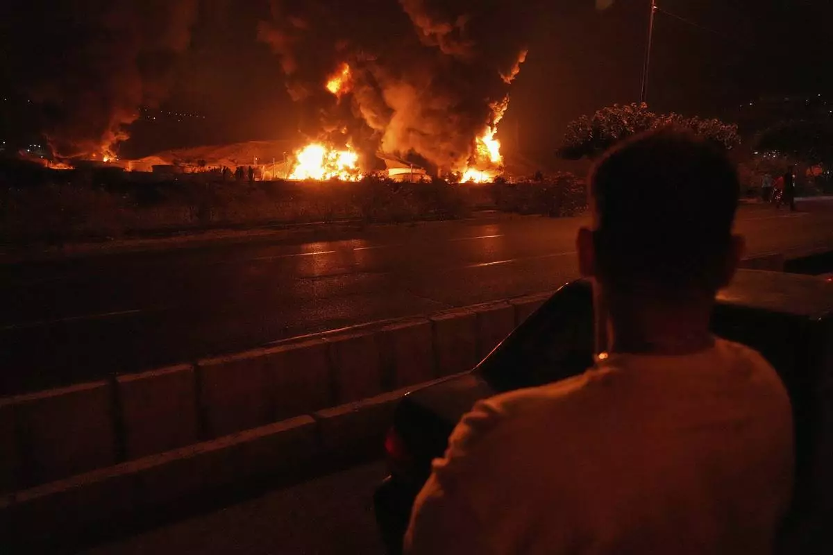A man looks at flames rising from an oil storage facility after it was hit by an Israeli strike in Tehran, Iran, early Sunday, June 15, 2025. (AP Photo/Vahid Salemi)