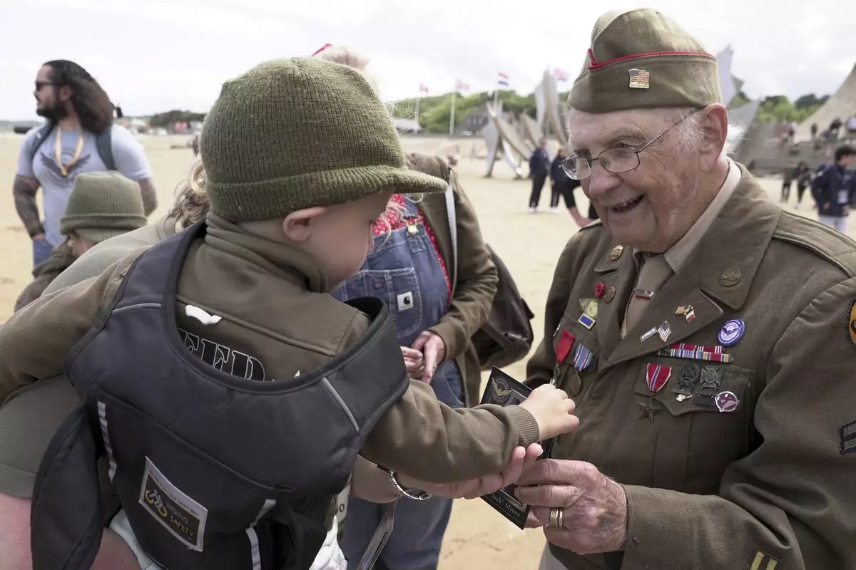 World War II veteran Wilbur "Jack" Myers, a 101-year-old who fought in the U.S. Army's 692nd Tank Destroyer Battalion, hands a souvenir postcard of himself to Ryan, a young French boy, on Monday, June 2, 2025, at Omaha beach, which was one of the D-D-day invasion spots on June 6, 1944. (AP Photo/John Leicester)