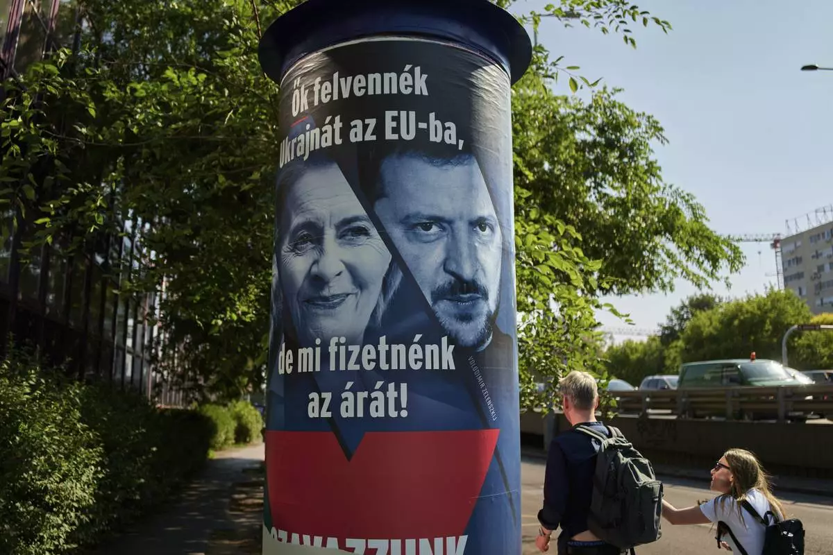 People pass by a Hungarian government billboard, opposing Ukraine's EU membership, showing European Commission President Ursula von der Leyen and Ukrainian President Volodymyr Zelenskyy, which reads "They would bring Ukraine into the EU, but we would pay the price! Let's vote no!", In Budapest, Hungary, Wednesday, June 11, 2025. (AP Photo/Bela Szandelszky)
