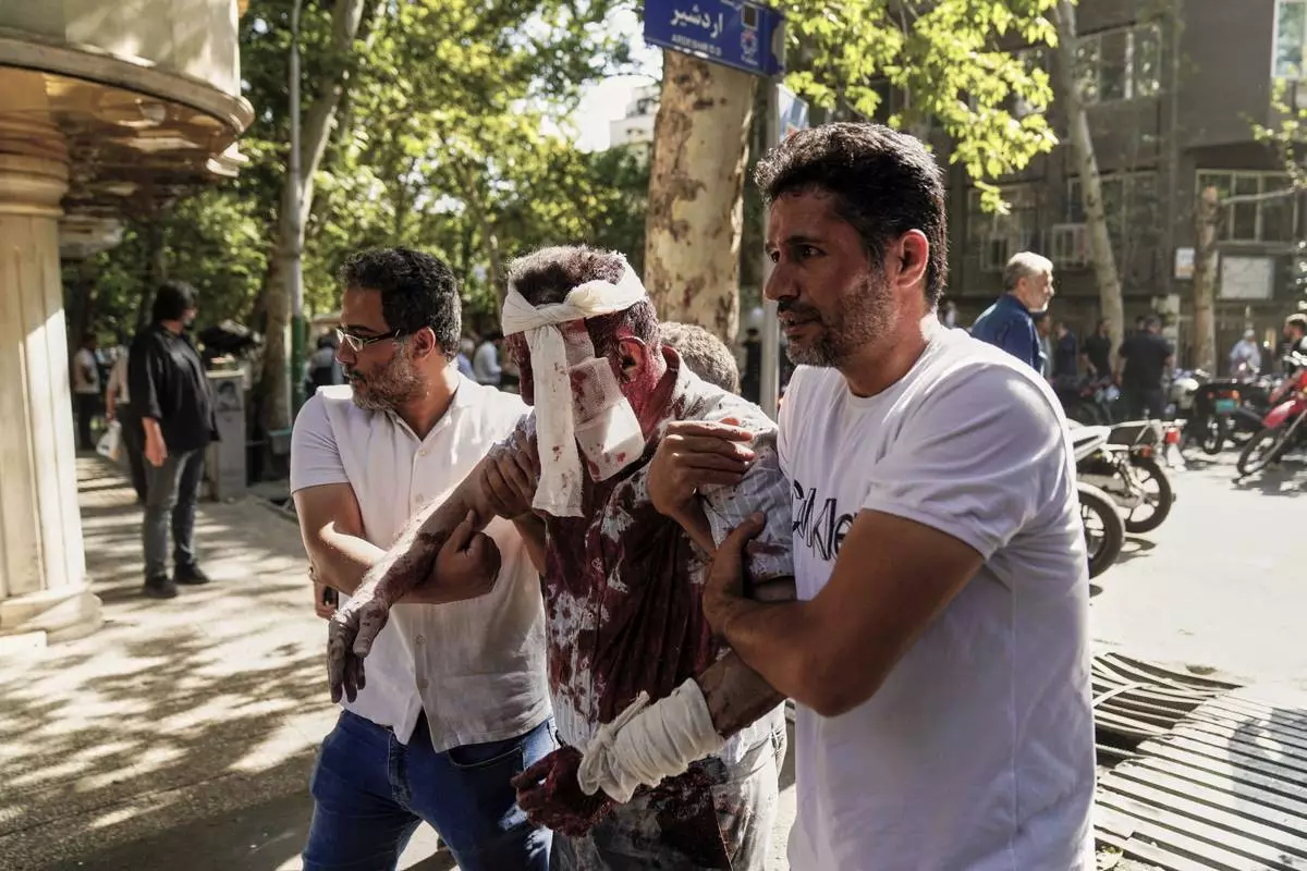 An injured man is helped to leave the scene after an explosion in downtown Tehran, amid Israel's three-day campaign of strikes against Iran, Sunday, June 15, 2025. (AP Photo/Amir Kholousi/ISNA)