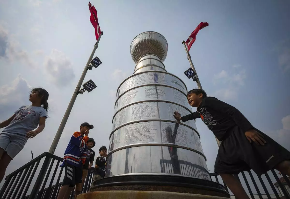Kids from Pierceland, Saskatchewan, in the city on vacation, stop to touch and look at a nearly 4 meter replica of the Stanley Cup trophy, Tuesday, June 3, 2025, that is a permanent installation in Edmonton, Alberta, ahead of Game 1 of the NHL hockey Stanley Cup final series between the Florida Panthers the Edmonton Oilers. (Darryl Dyck/The Canadian Press via AP)