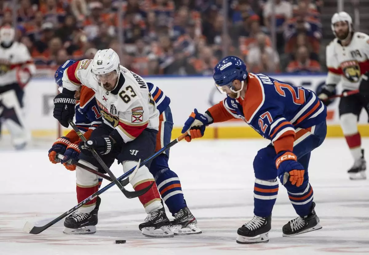 Florida Panthers' Brad Marchand (63) and Edmonton Oilers' Brett Kulak (27) battle for the puck during the third period in Game 1 of the NHL hockey Stanley Cup final series in Edmonton, Alberta, Wednesday, June 4, 2025. (Jason Franson/The Canadian Press via AP)