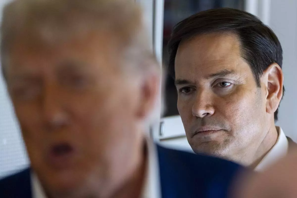 Secretary of State Marco Rubio stands behind as President Donald Trump speaks with reporters on Air Force One while in flight from Joint Base Andrews, Md., to Amsterdam, Netherlands, Tuesday, June 24, 2025. (AP Photo/Alex Brandon)