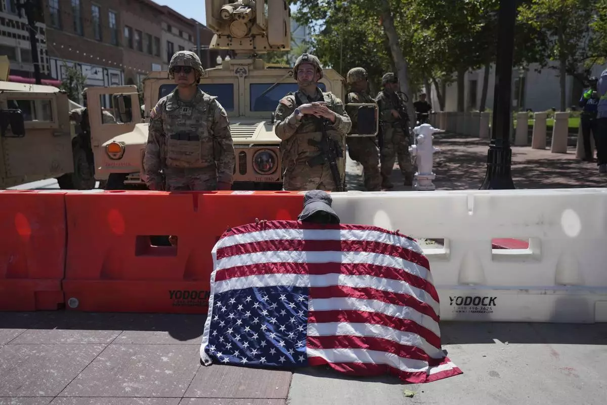 Protester Annie Jones holds a U.S. Flag upside down as a sign of distress while California National Guard stand behind a barricade in Santa Ana, Calif. on Tuesday, June 10, 2025. (AP Photo Jae C. Hong)