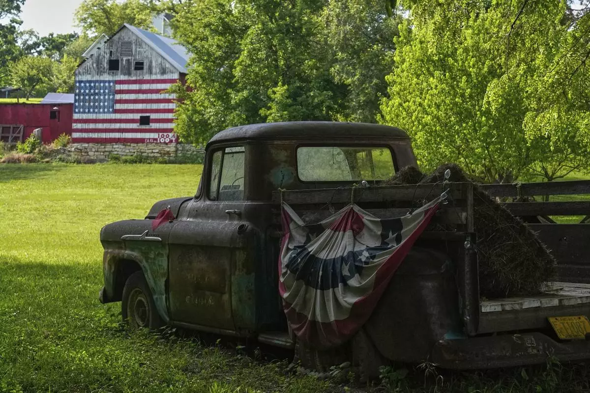 A flag-painted barn stands in the distance beyond an old pickup truck Saturday, June 7, 2025, on the a farm owned by Quentin and Karrie Brewer near Loring, Kan. The barn was painted by Quentin, who's birthday is flag day, with 38 stars representing the number of states in the union when the barn was built in 1884. (AP Photo/Charlie Riedel)