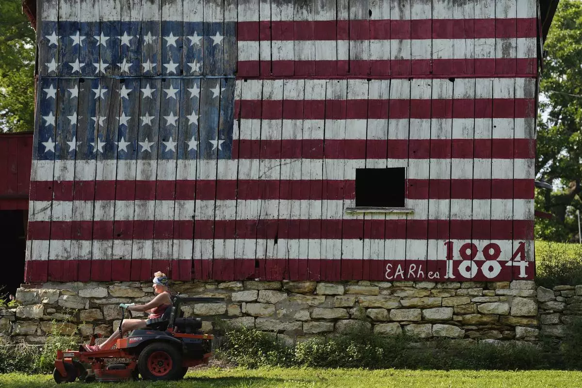Karrie Brewer mows in front of a flag-painted barn Saturday, June 7, 2025, on the family farm near Loring, Kan. The barn was painted by her husband, Quentin Brewer, who's birthday is flag day, with 38 stars representing the number of states in the union when the barn was built in 1884. (AP Photo/Charlie Riedel)