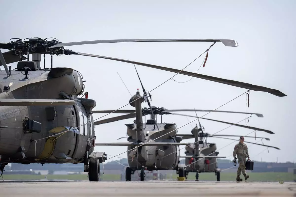 A crew member walks past U.S. Army UH-60M Black Hawk helicopters that will participate in an upcoming military parade commemorating the Army's 250th anniversary and coinciding with President Donald Trump's 79th birthday, at Joint Base Andrews, Md., Thursday, June 12, 2025. (AP Photo/Mark Schiefelbein)