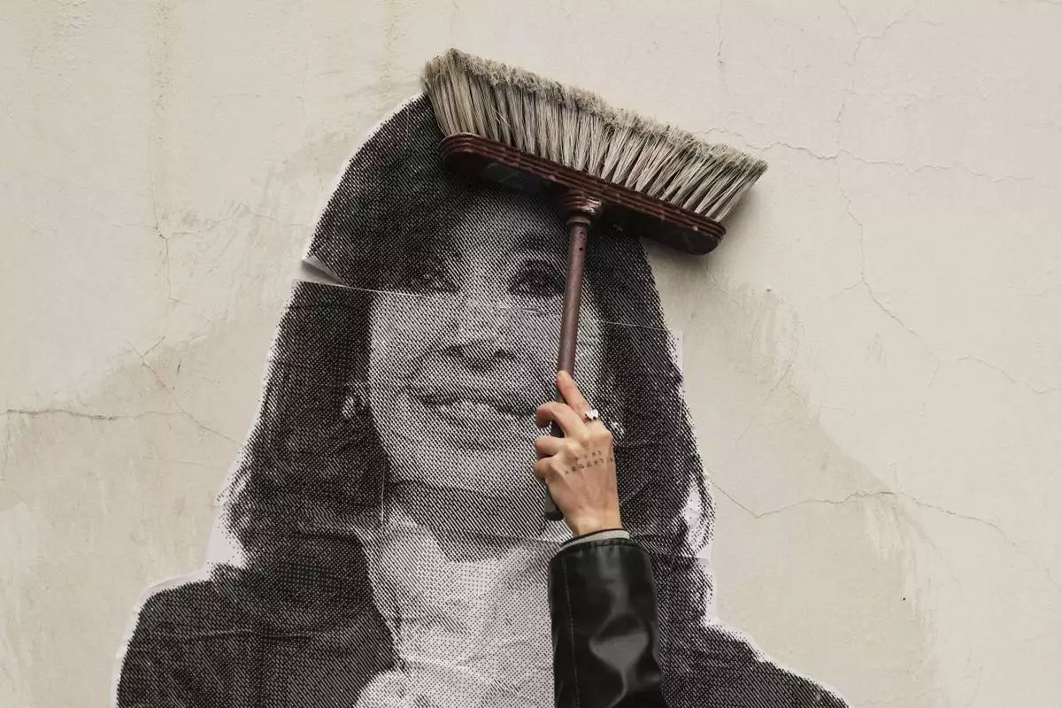 A supporter of Argentina's former President Cristina Fernandez uses a broom to paste a photo of her on the wall outside her home in Buenos Aires, Argentina, Tuesday, June 17, 2025. (AP Photo/Natacha Pisarenko)