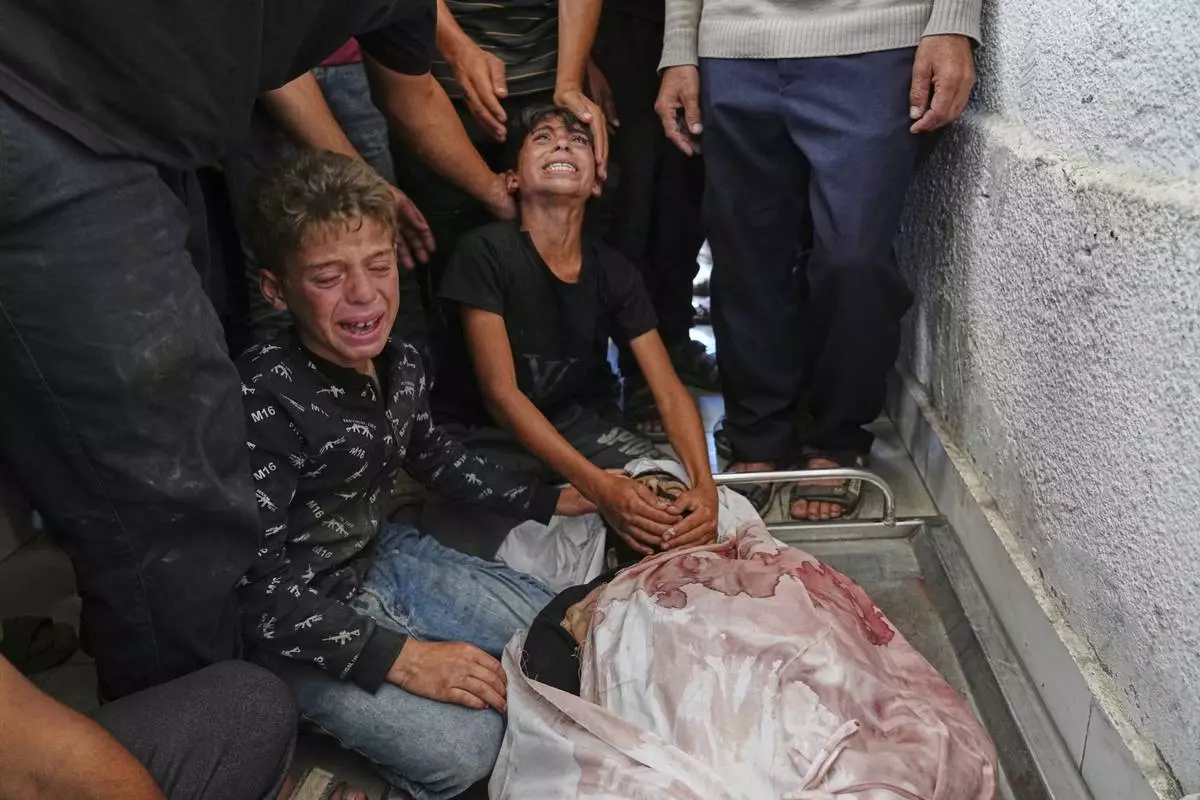 Palestinian children mourn over the body of their father, Mohammed Ghaben, who was killed while heading to an aid distribution hub, in Gaza City, Wednesday, June 18, 2025. (AP Photo/Jehad Alshrafi)