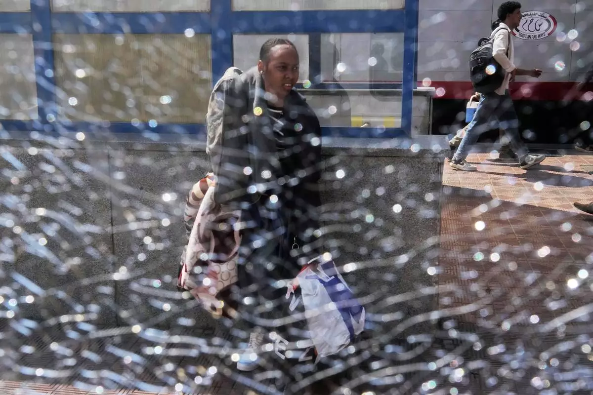 A Sudanese woman, who was driven from her home and is now returning, is seen though a broken window as she waits for her train to Aswan at Cairo's Ramses railway station, Egypt, Monday, July 21, 2025. (AP Photo/Amr Nabil)
