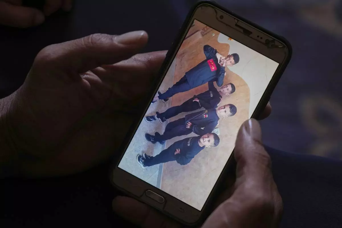 Hatem Al-Nouri shows a photo of his children Amir, 4, right, and Omar, 8, second from right, accompanied by their brothers, as he talks about when Hatem and Amir were killed in an Israeli strike while waiting to receive nutritional supplements at a medical clinic, during an interview at his home in Deir al-Balah, Gaza Strip, Friday, July 11, 2025. (AP Photo/Abdel Kareem Hana)