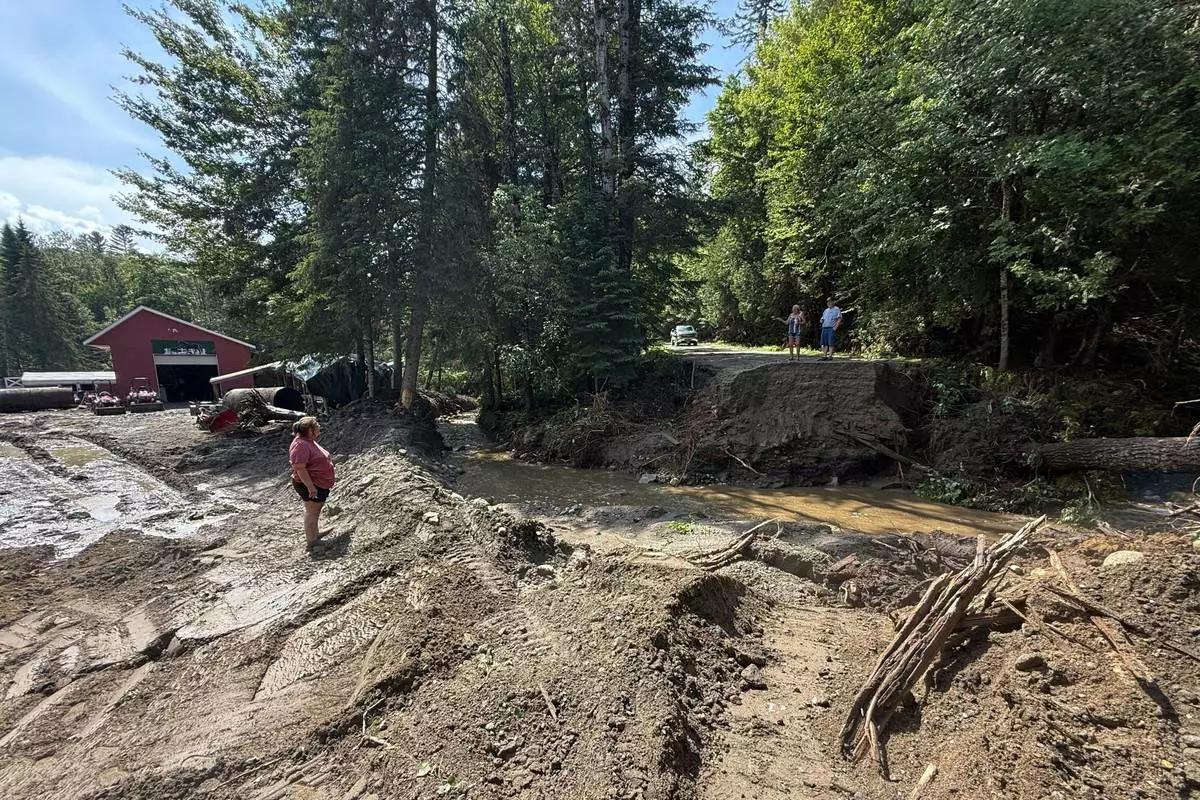 Michelle Tanner, whose yard was washed away by flash flooding, stands in what used to be her driveway as she talks with neighbors on a destroyed roadway, Friday, July 11, 2025 in Sutton, Vt. (AP Photo/Amanda Swinhart)