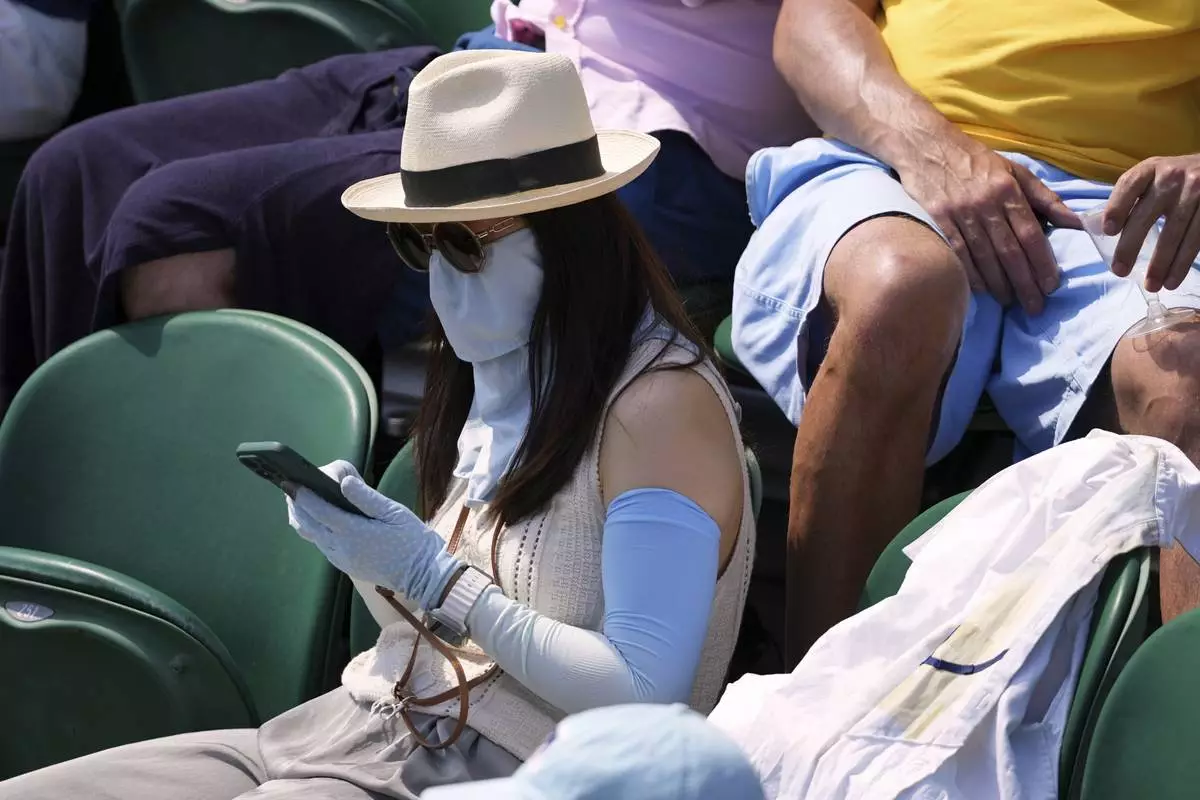 A woman protects her arms and face from the sun as she sits in the crowd to watch the Wimbledon Tennis Championships in London, Monday, June 30, 2025. (AP Photo/Kirsty Wigglesworth)