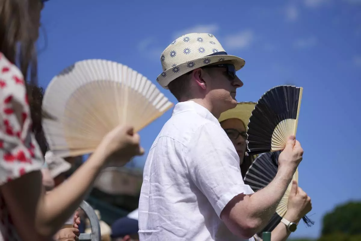 Visitors use fans to stay cool at the Wimbledon Tennis Championships in London, Monday, June 30, 2025. (AP Photo/Kin Cheung)