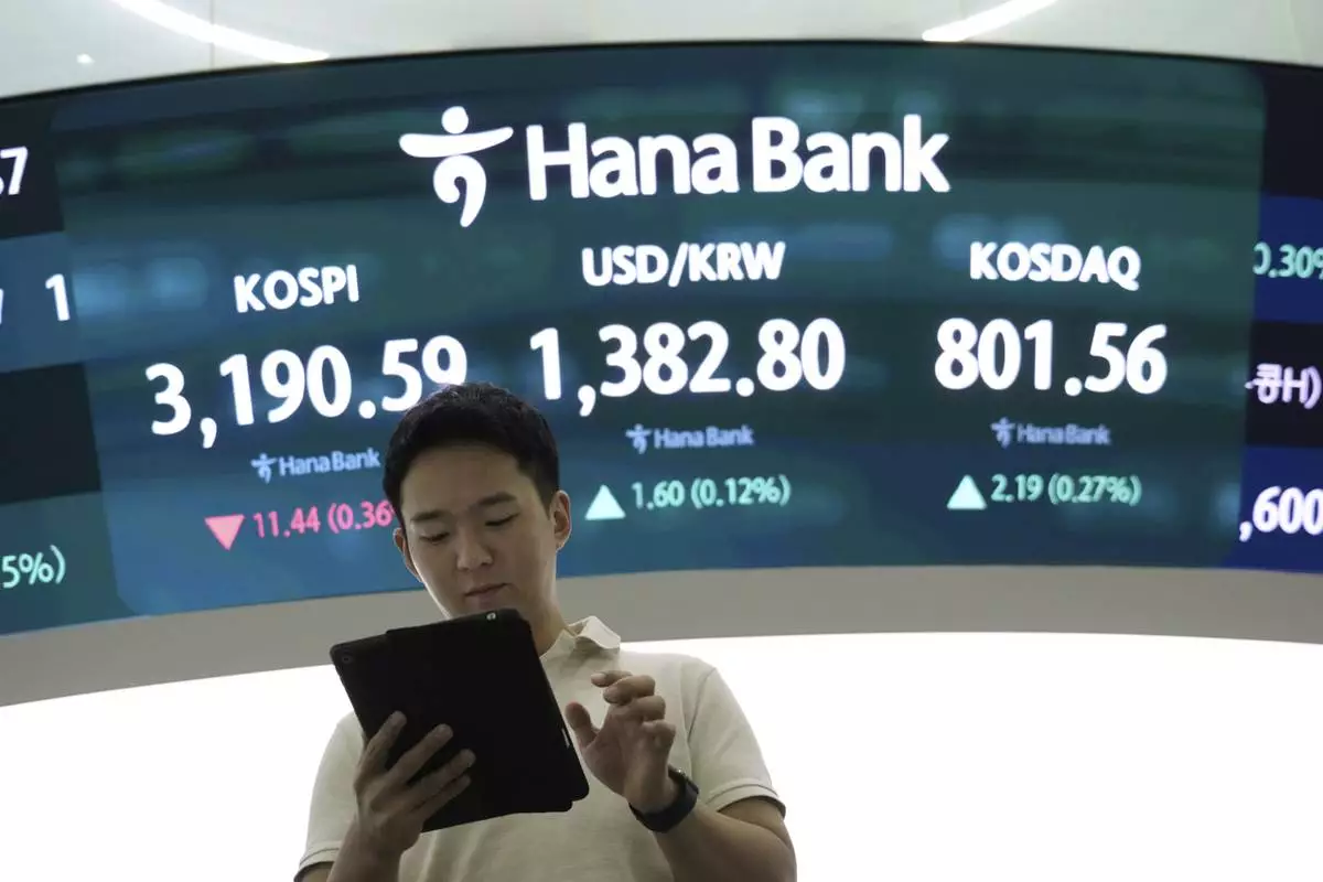 A currency trader works near a screen showing the Korea Composite Stock Price Index (KOSPI), top left, and the foreign exchange rate between U.S. dollar and South Korean won, top center, at the foreign exchange dealing room of the Hana Bank headquarters in Seoul, South Korea, Tuesday, July 15, 2025. (AP Photo/Ahn Young-joon)