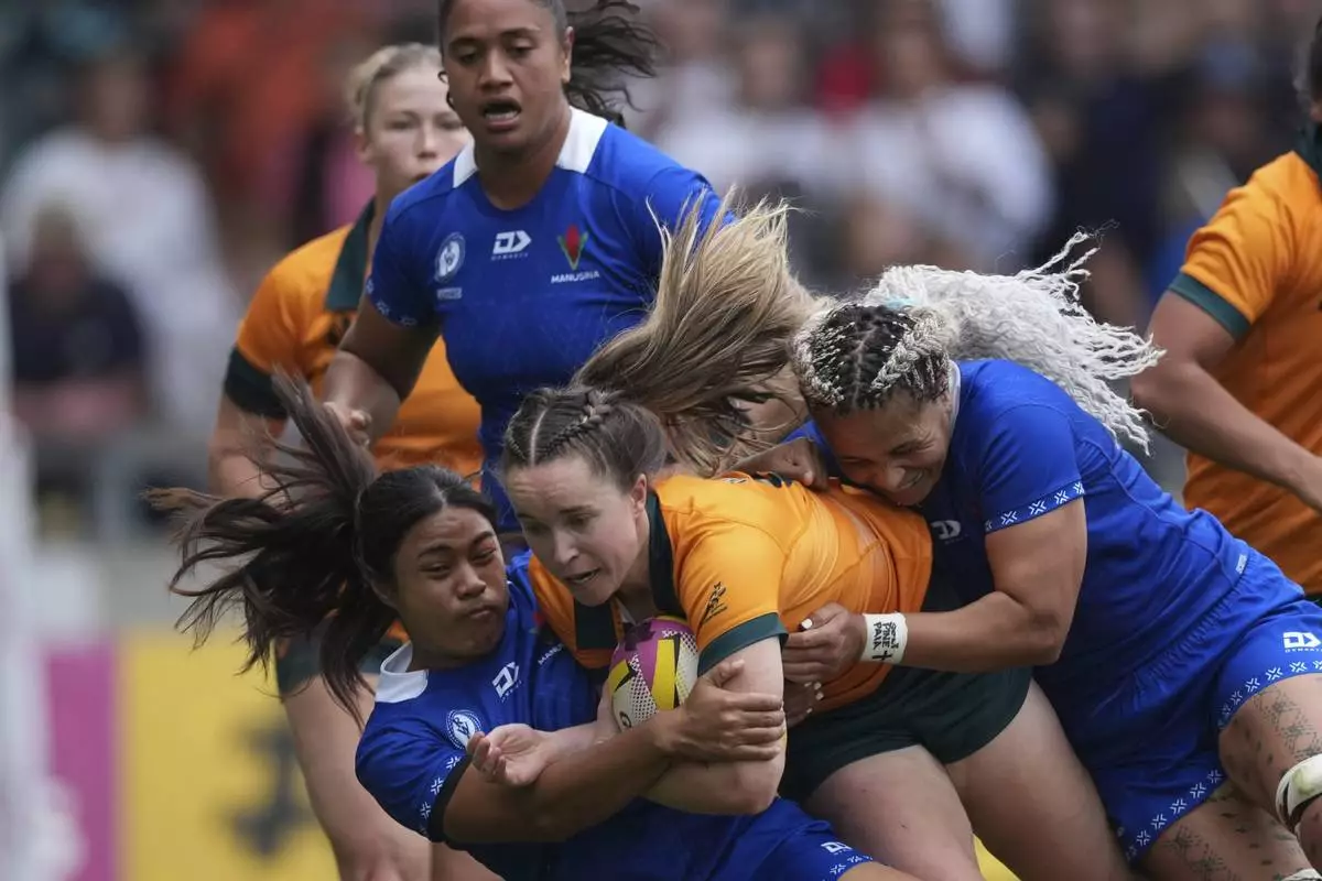 Tia Hinds of Australia, center, is tackled by Sui Pauaraisa of Samoa during the group A match at the 2025 Women's Rugby World Cup between Australia and Samoa in Manchester, England, Saturday, Aug. 23, 2025. (AP Photo/Dave Shopland)