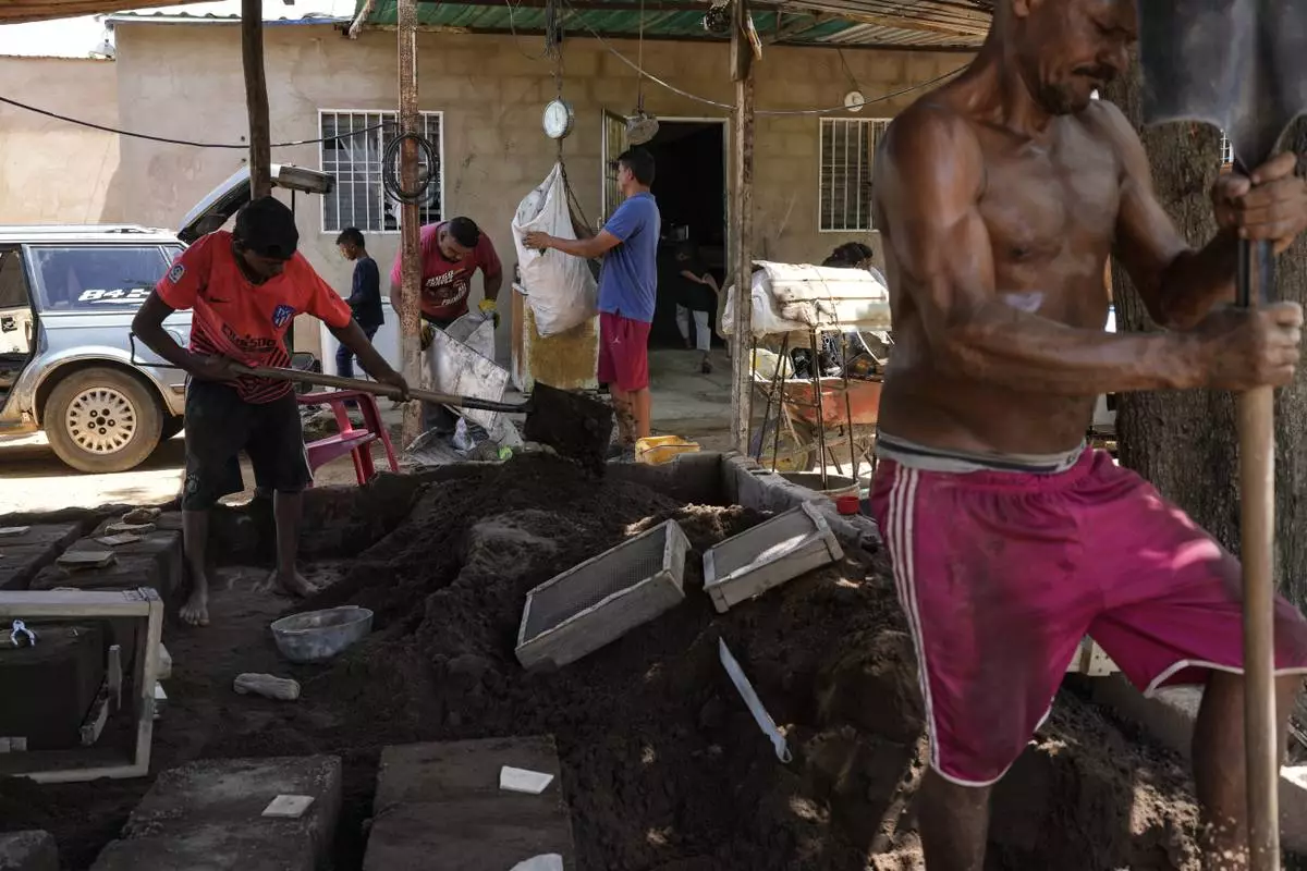 Jolber Romero, left, one of five children who returned to Venezuela from Mexico with his parents after abandoning plans to reach the United States amid President Donald Trump's migration crackdown, shovels sand into molds to cast aluminum pots, in Maracaibo, Venezuela, Monday, June 16, 2025. (AP Photo/Matias Delacroix)