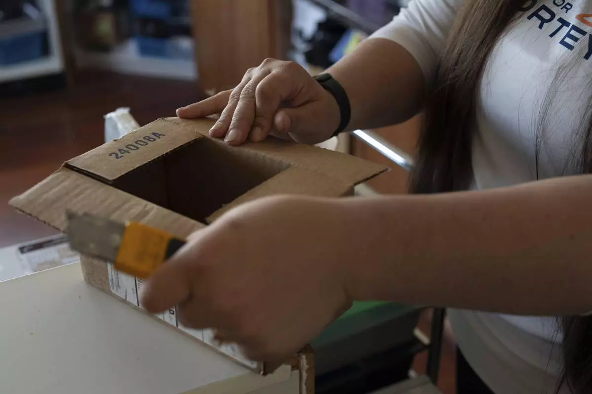 Amanda Follett opens packages at A Sight For Sore Eyes, a brick-and-mortar and ecommerce store for sport goggles, Wednesday, Aug. 20, 2025, in West Linn, Ore. (AP Photo/Jenny Kane)