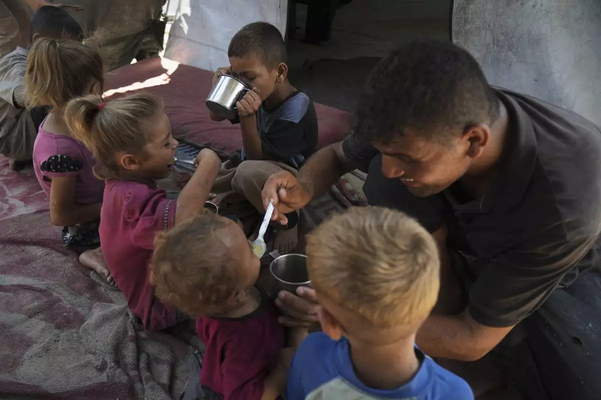 Fadi Sobh gives lentil soup to his children as they sit in their tent at a camp for displaced Palestinians in Gaza City, Thursday, July 24, 2025. (AP Photo/Jehad Alshrafi)