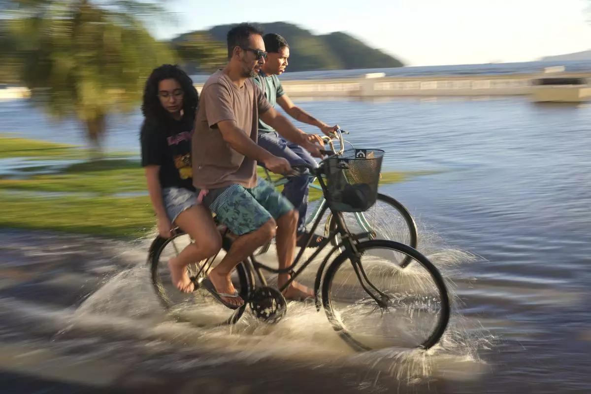 A family rides bicycles along a bike path flooded by ocean water in Santos, Brazil, July 29, 2025. (AP Photo/Andre Penner)