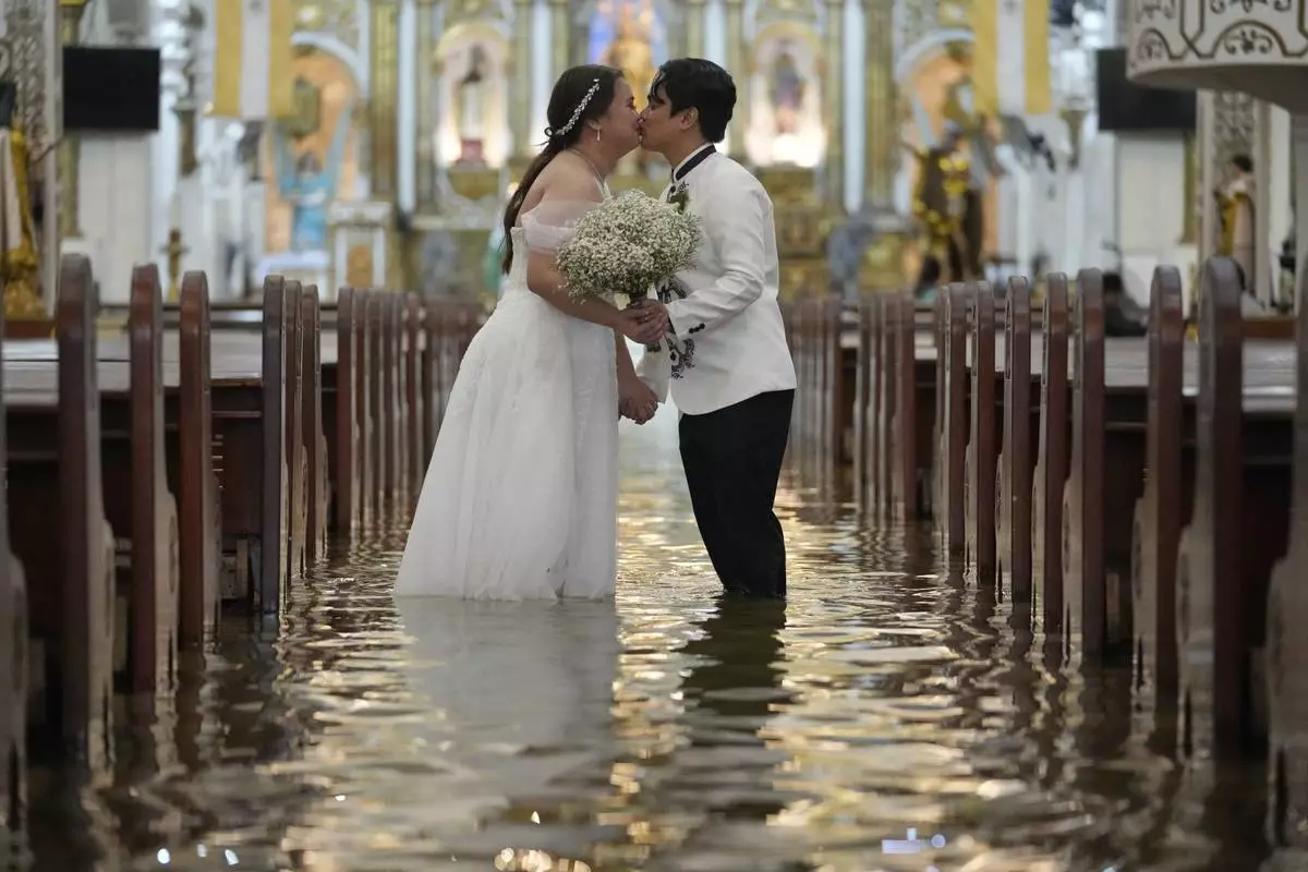 Newlyweds Jade Rick Verdillo, right, and Jamaica kiss during their wedding inside a flooded Barasoain church in Malolos, Philippines, July 22, 2025. (AP Photo/Aaron Favila)