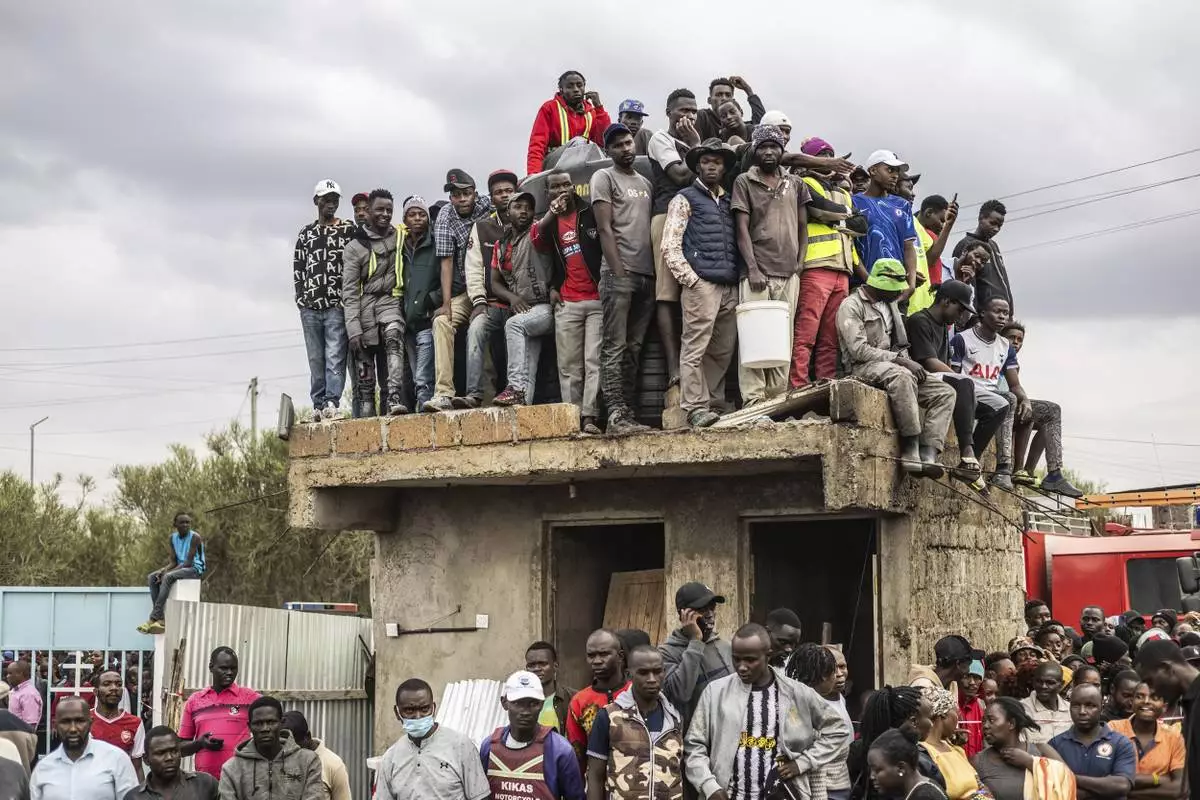 People gather on a rooftop to get a view of the site where a plane belonging to an air ambulance service provider crashed into a residential area killing several people, in the Mwihoko area of Ruiru, just outside Kenya's capital, Aug. 7, 2025. (AP Photo/Samson Otieno)