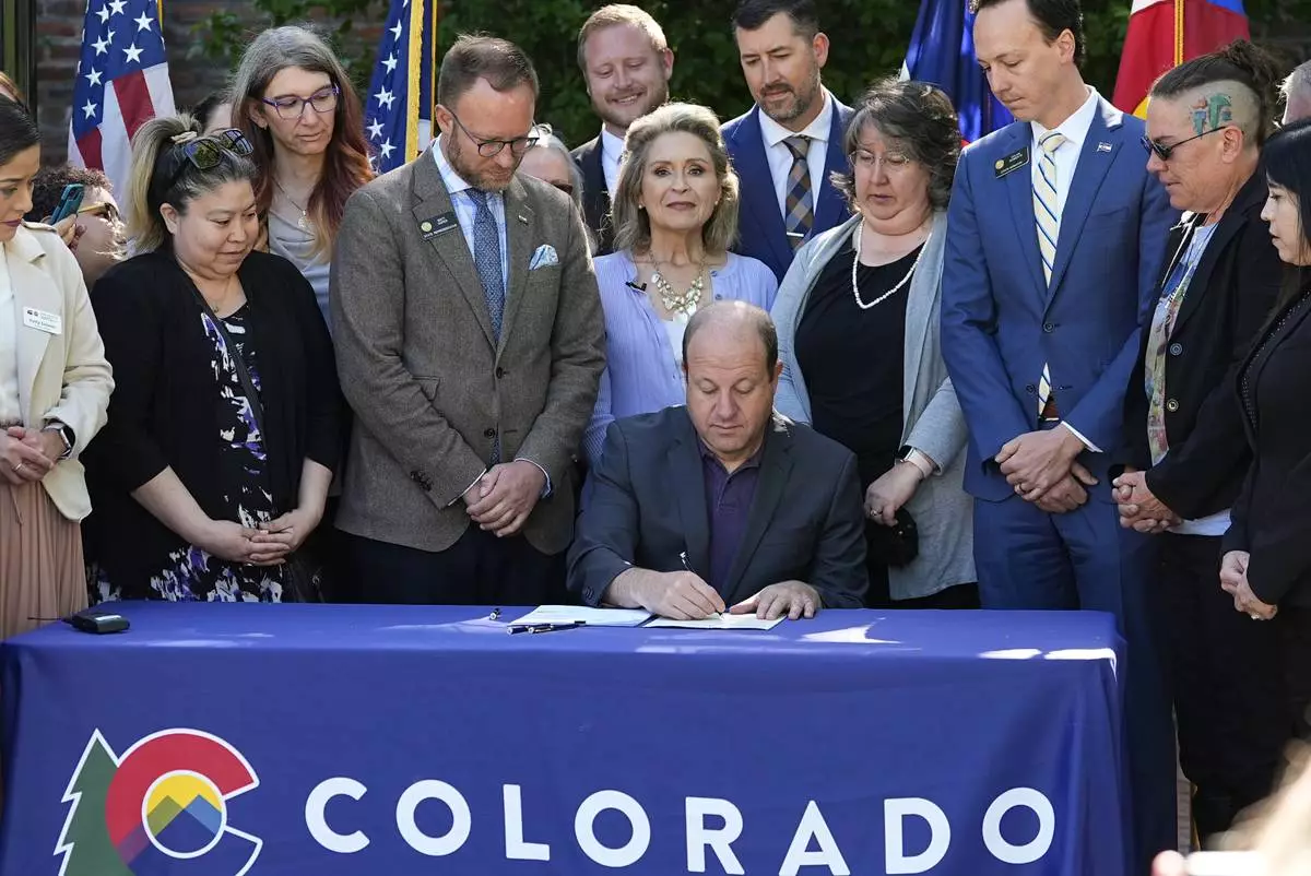 FILE - Colorado Gov. Jared Polis, front center, signs bills into law to bring more comprehensive guidelines into place for funeral facilities on May 24, 2024, during a ceremony outside the Governor's mansion in downtown Denver. (AP Photo/David Zalubowski, File)