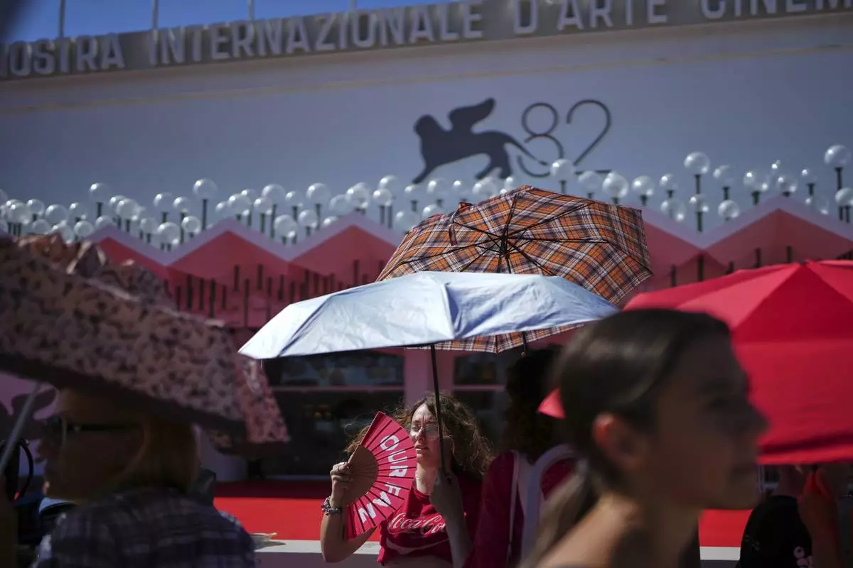 Festival goers shelter from the sun as they wait for arrivals on the red carpet for the film 'The Wizard of the Kremlin' during the 82nd edition of the Venice Film Festival in Venice, Italy, on Sunday, Aug. 31, 2025. (Photo by Alessandra Tarantino/Invision/AP)
